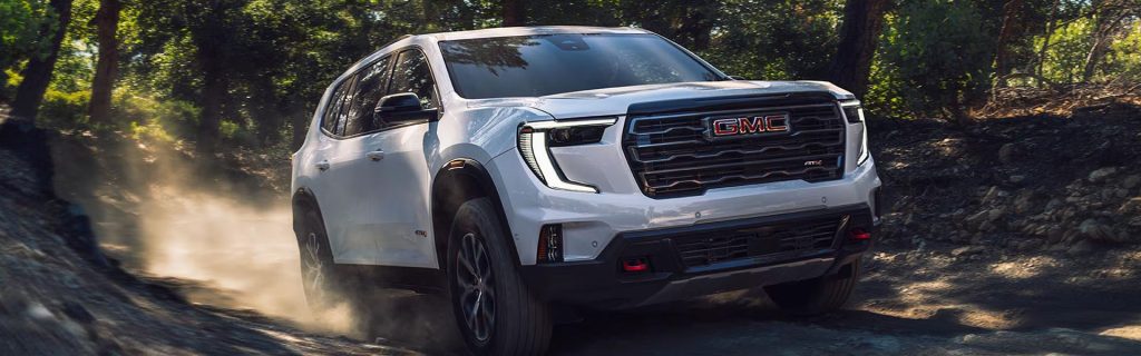 2026 GMC Acadia AT4 SUV driving on a dirt trail near Coldwater, MI, featuring off-road performance, bold exterior styling, and advanced capability.